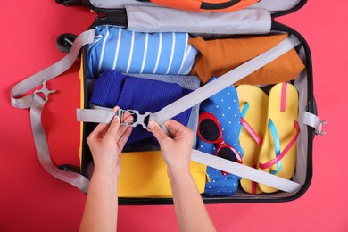 Photo of Traveler packing suitcase on red background, top view