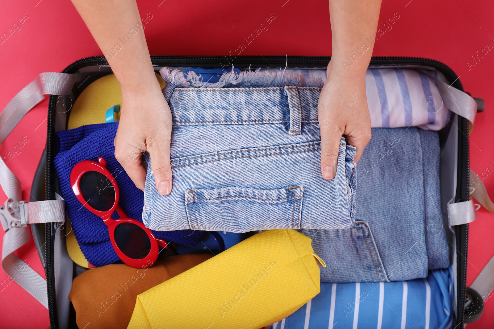 Photo of Traveler packing suitcase on red background, top view