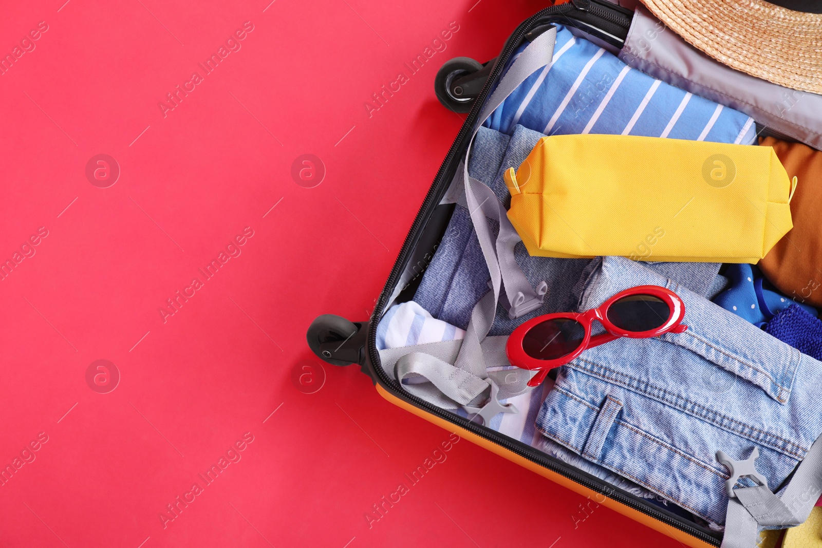 Photo of Travel abroad. Packed suitcase on red background, top view. Space for text