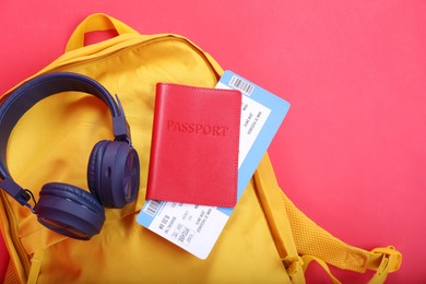 Photo of Backpack, headphones and passport with ticket on red background, closeup. Travel abroad