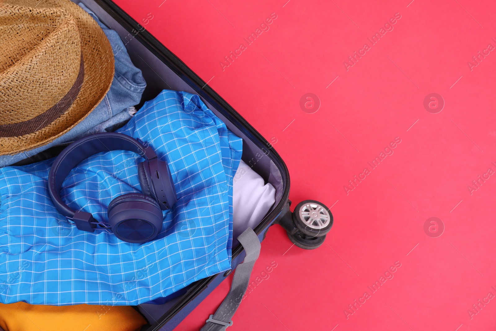 Photo of Travel abroad. Packed suitcase on red background, above view. Space for text