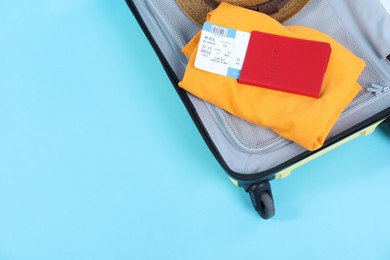 Photo of Travel abroad. Packed suitcase with passport and ticket on light blue background, top view. Space for text