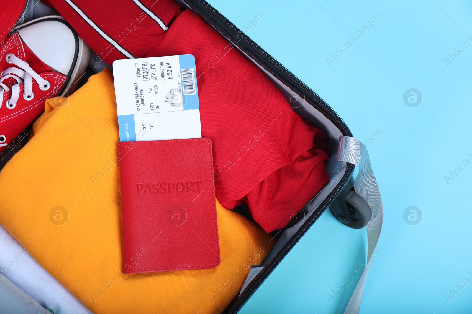 Photo of Travel abroad. Packed suitcase with passport and ticket on light blue background, top view