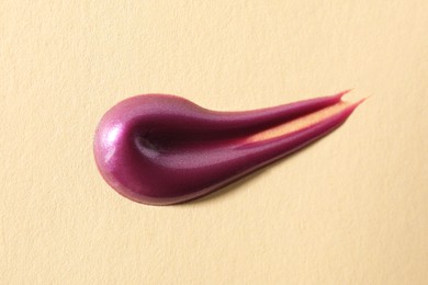 Photo of Sample of purple lipgloss on beige background, above view