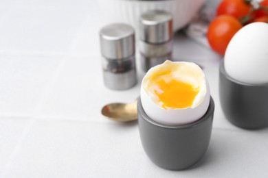 Photo of Soft boiled eggs in cups served on white tiled table, closeup. Space for text