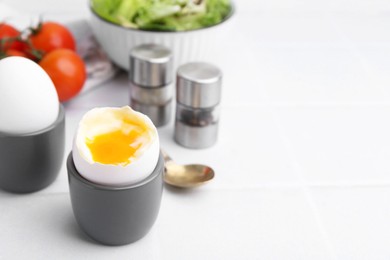 Photo of Soft boiled eggs in cups served on white tiled table, closeup. Space for text