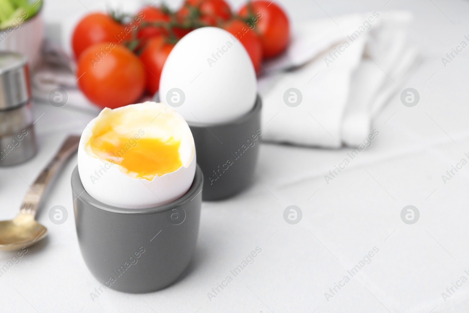 Photo of Soft boiled eggs in cups served on white tiled table, closeup. Space for text