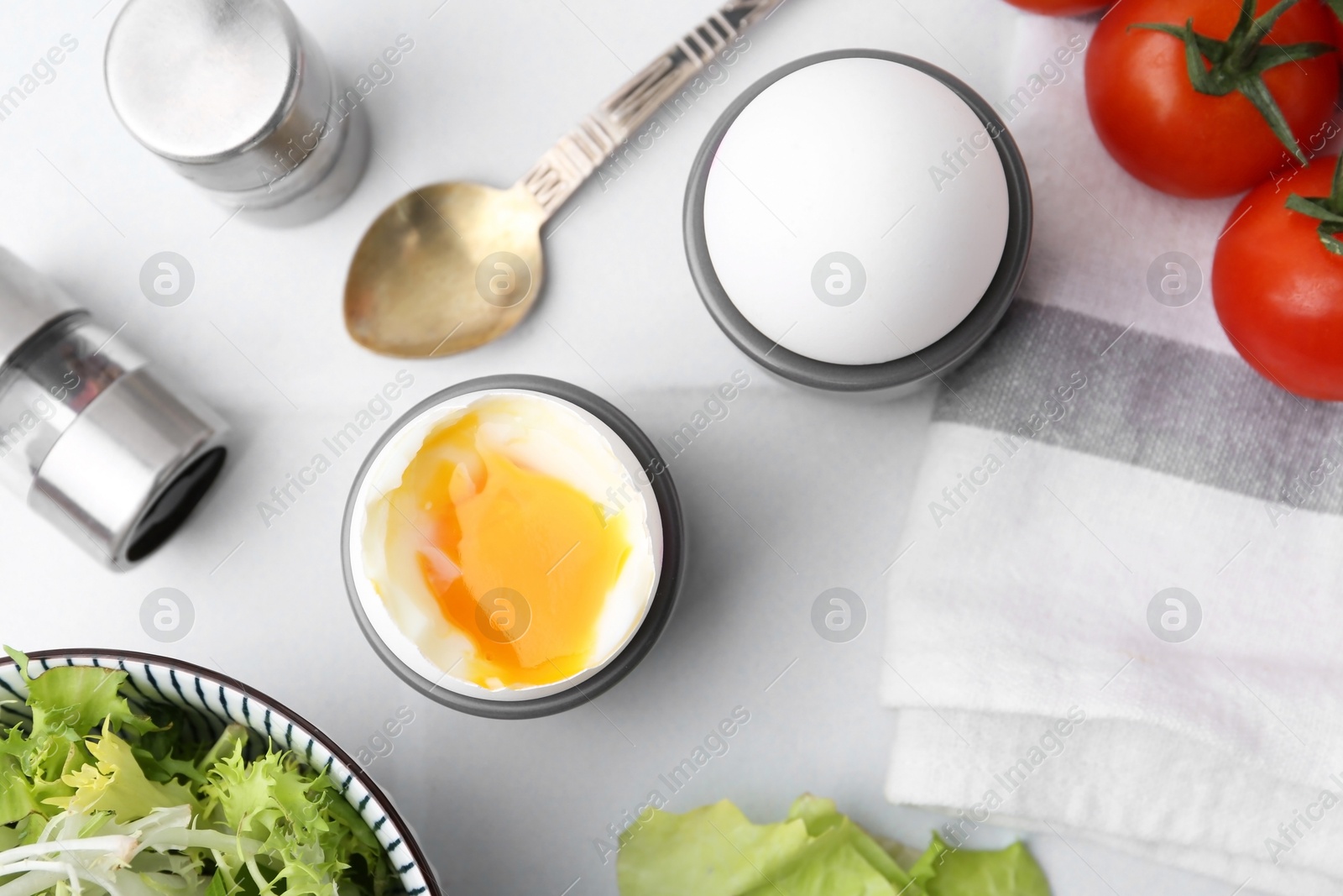 Photo of Soft boiled eggs in cups served on white tiled table, flat lay