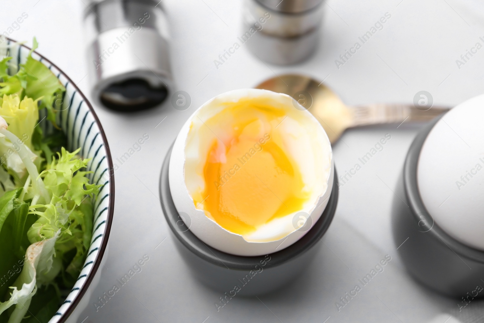 Photo of Soft boiled eggs in cups served on white tiled table, closeup