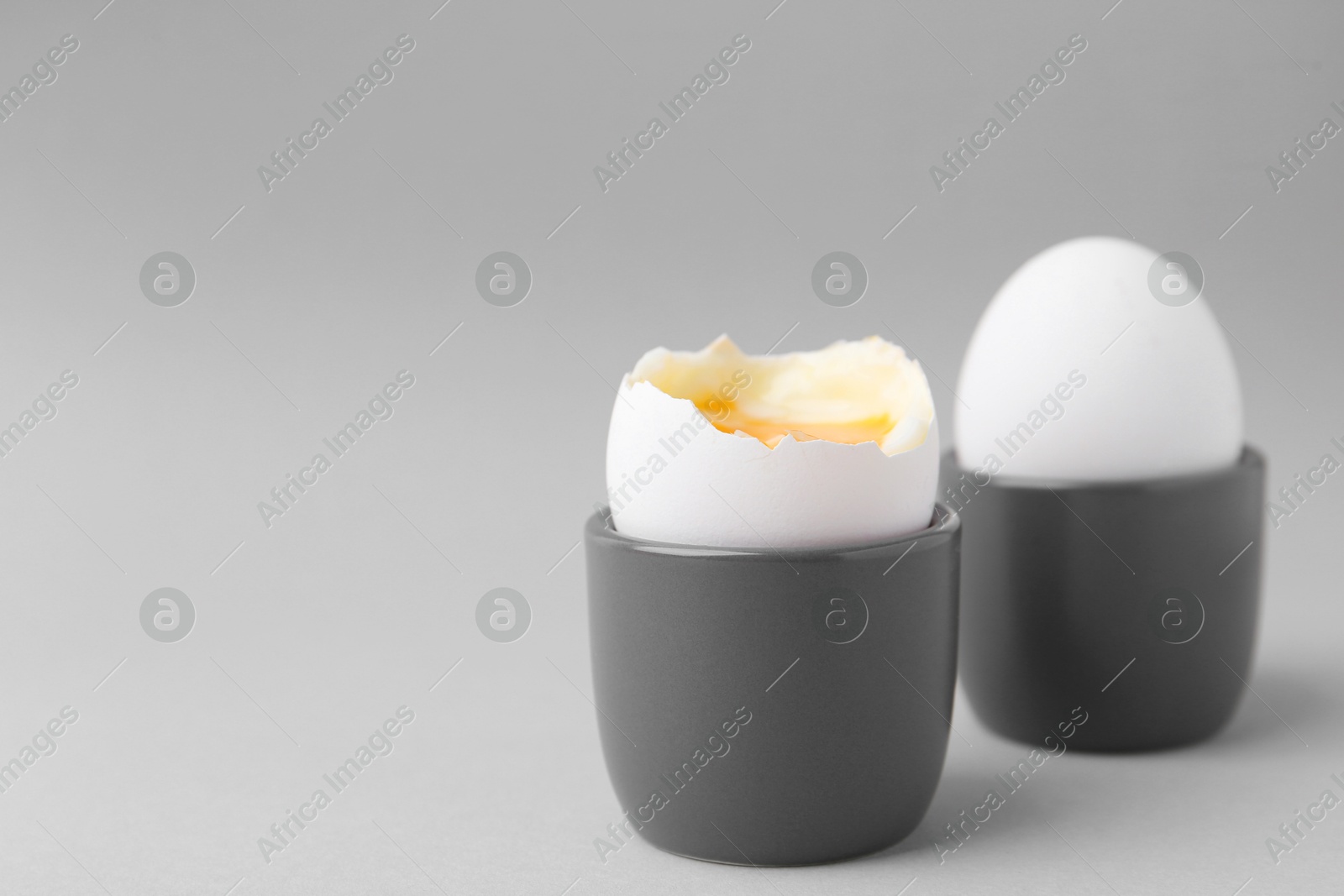 Photo of Soft boiled eggs in cups on light grey background, closeup. Space for text