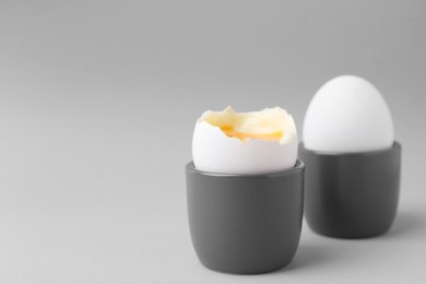 Photo of Soft boiled eggs in cups on light grey background, closeup. Space for text