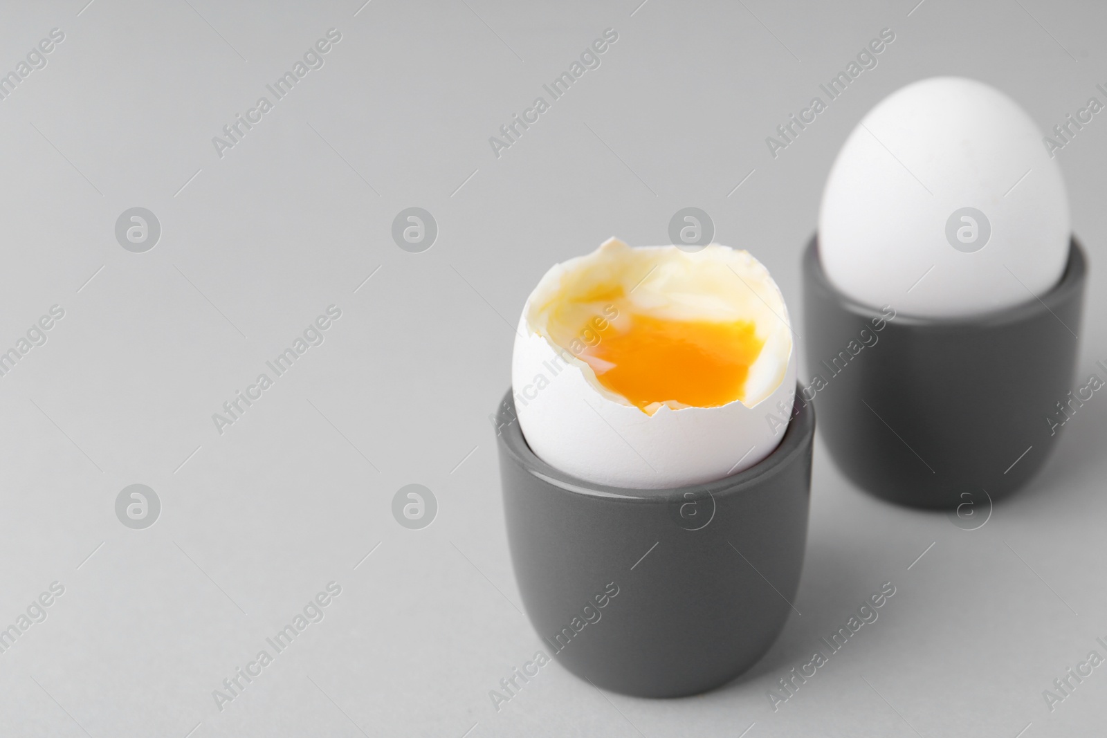 Photo of Soft boiled eggs in cups on light grey background, closeup. Space for text