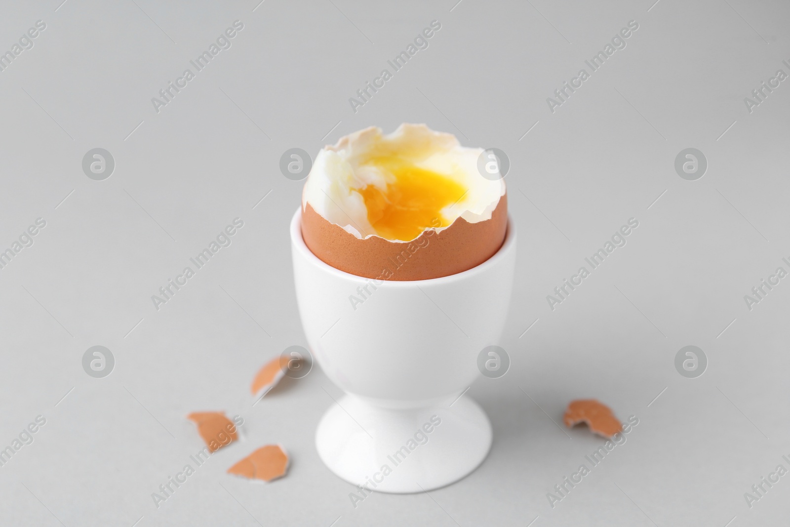 Photo of Soft boiled egg in cup and eggshell on light grey background