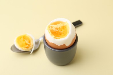 Photo of Soft boiled egg in eggcup and spoon on beige background, closeup