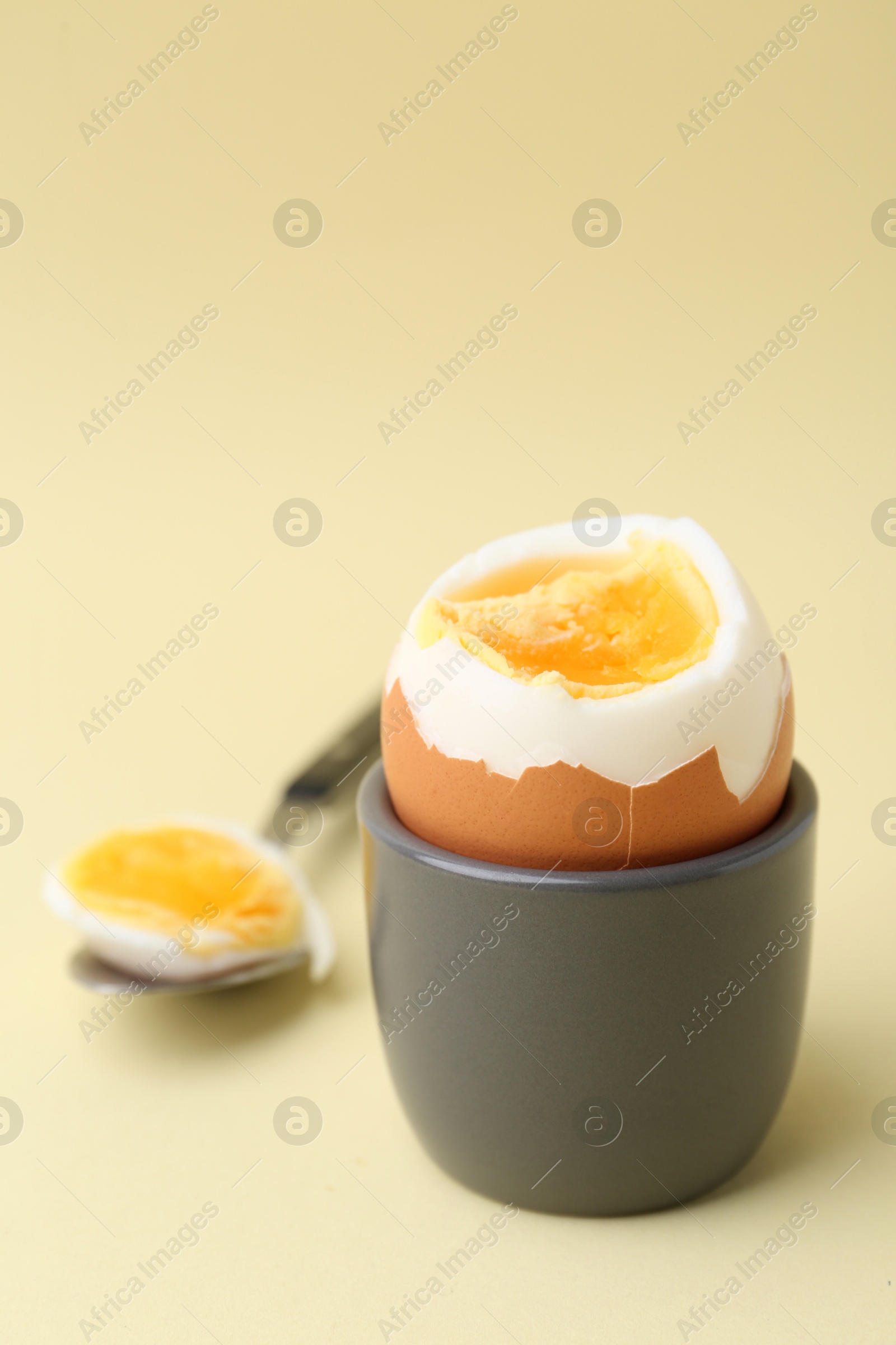 Photo of Soft boiled egg in eggcup and spoon on beige background, closeup