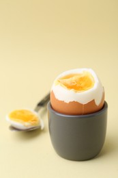 Photo of Soft boiled egg in eggcup and spoon on beige background, closeup