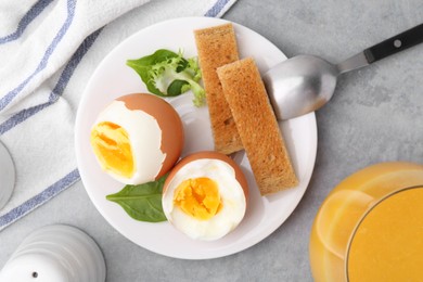 Soft boiled eggs with bread and juice on grey table, flat lay