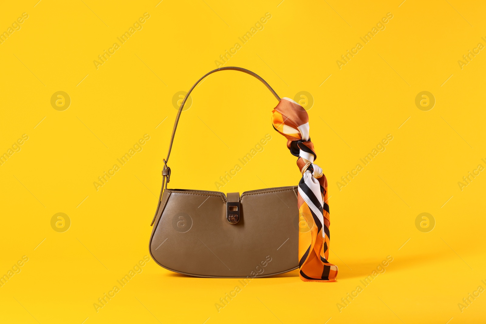 Photo of Stylish brown leather bag with handkerchief on yellow background