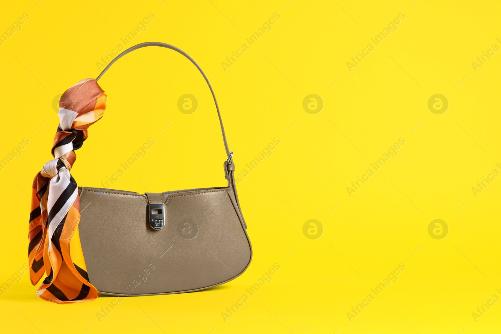 Photo of Stylish brown leather bag with handkerchief on yellow background, space for text