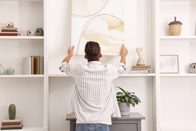 Photo of Male decorator hanging abstract picture indoors, back view