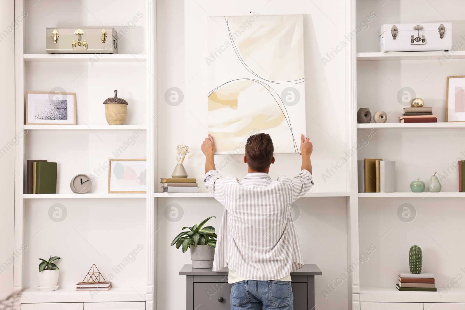 Photo of Male decorator hanging abstract picture indoors, back view