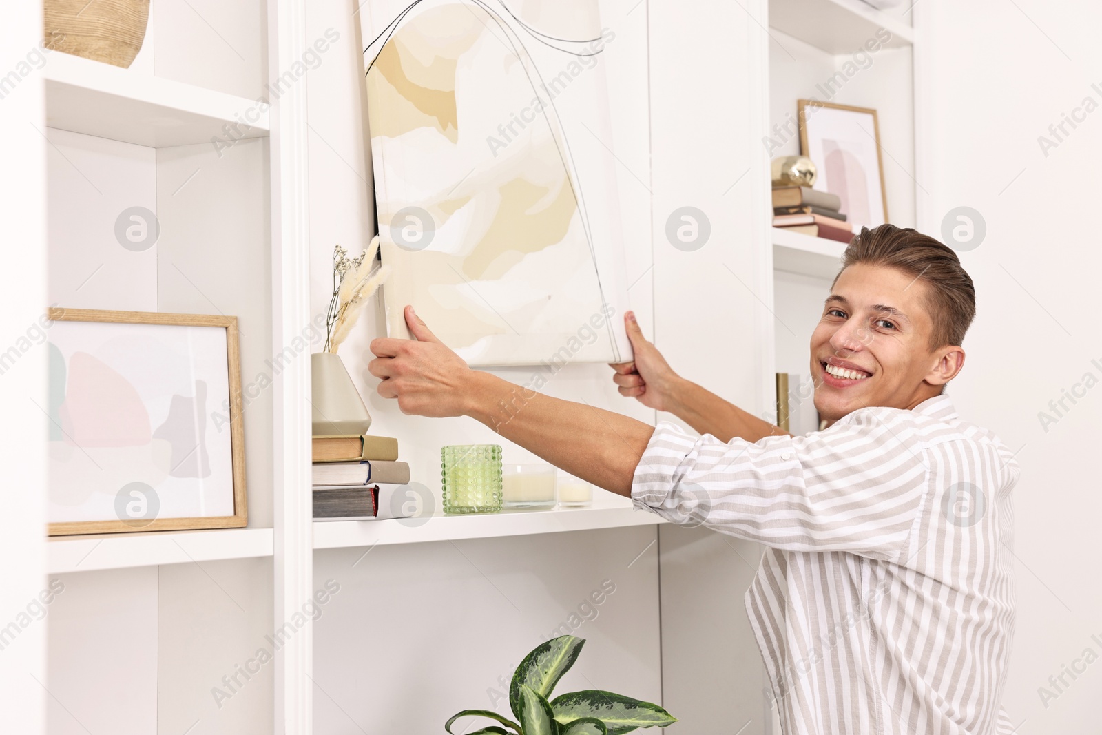 Photo of Smiling young decorator hanging abstract picture indoors