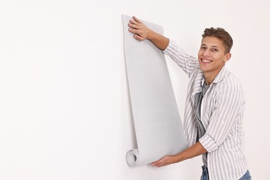 Photo of Smiling handyman hanging gray wallpaper indoors. Space for text