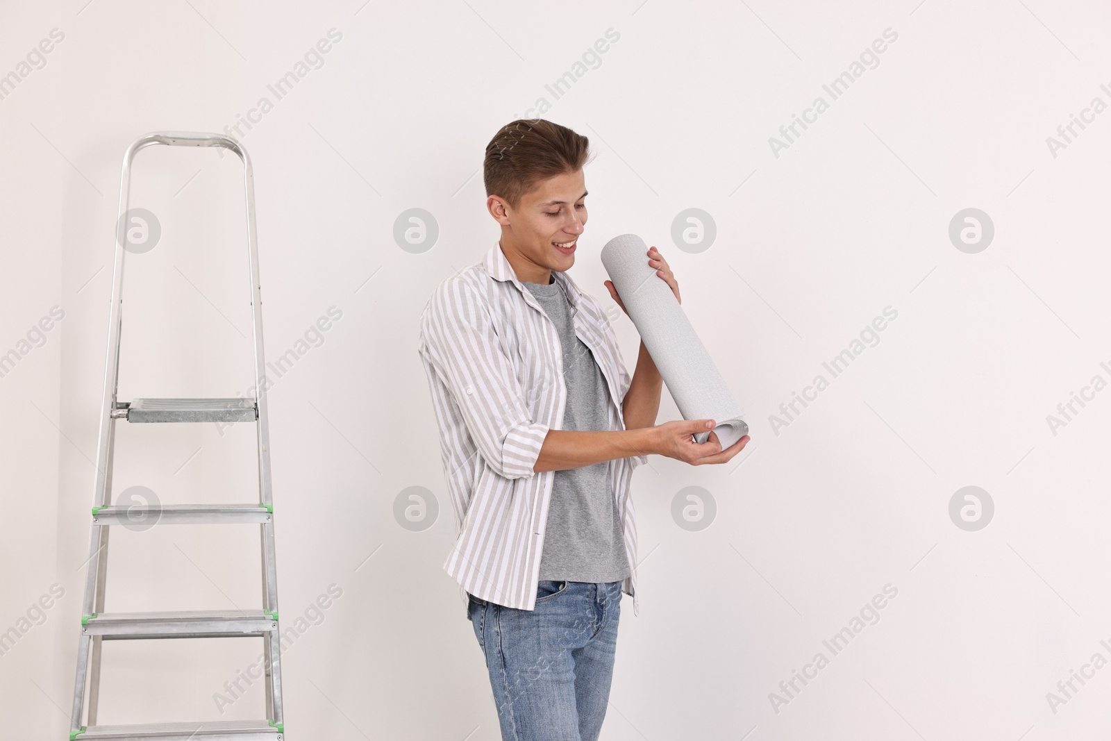 Photo of Smiling handyman with roll of wallpaper near ladder indoors