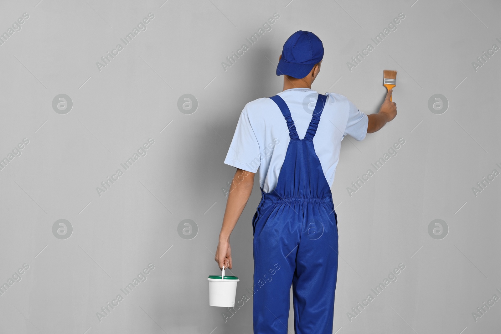 Photo of Male handyman painting wall with brush indoors, back view. Space for text