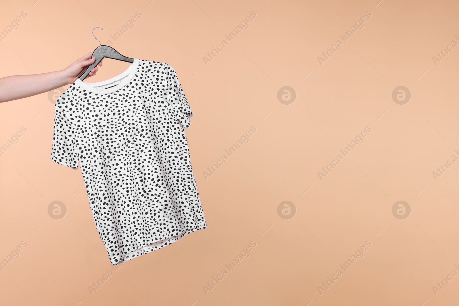 Photo of Woman holding hanger with t-shirt on beige background, closeup. Space for text