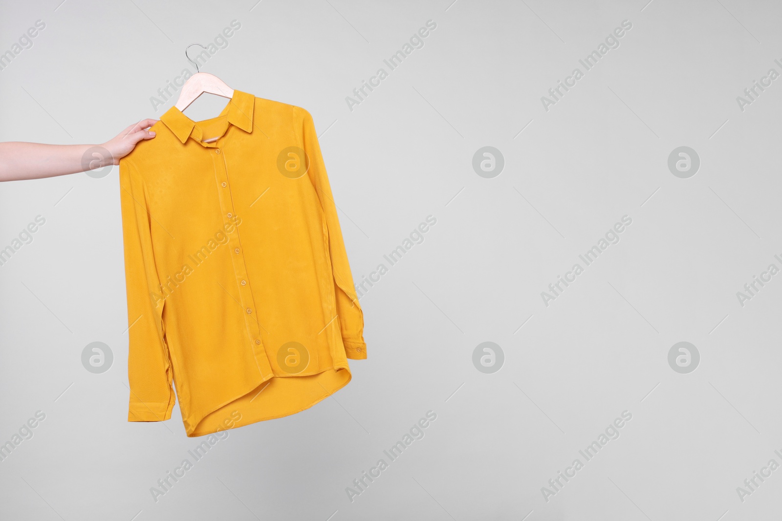 Photo of Woman holding hanger with orange shirt on light grey background, closeup. Space for text