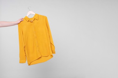 Photo of Woman holding hanger with orange shirt on light grey background, closeup. Space for text