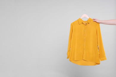 Photo of Woman holding hanger with orange shirt on light grey background, closeup. Space for text