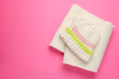 Photo of Warm woolen hat and scarf on pink background, top view. Space for text