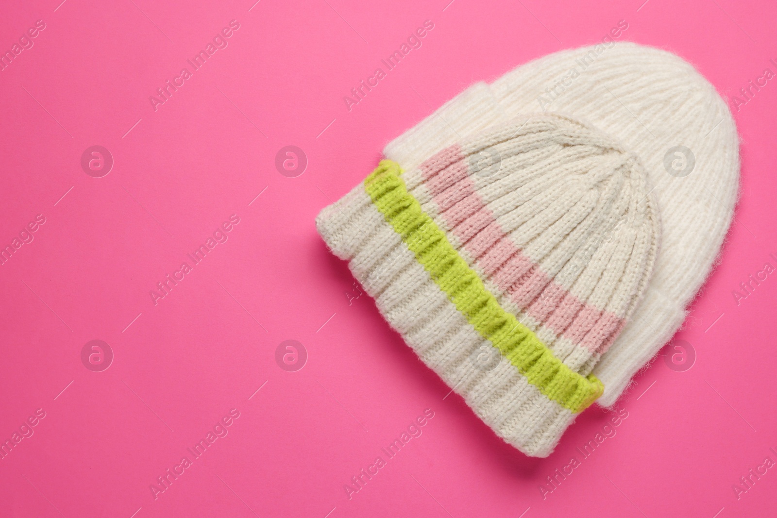 Photo of Warm woolen hats on pink background, top view. Space for text