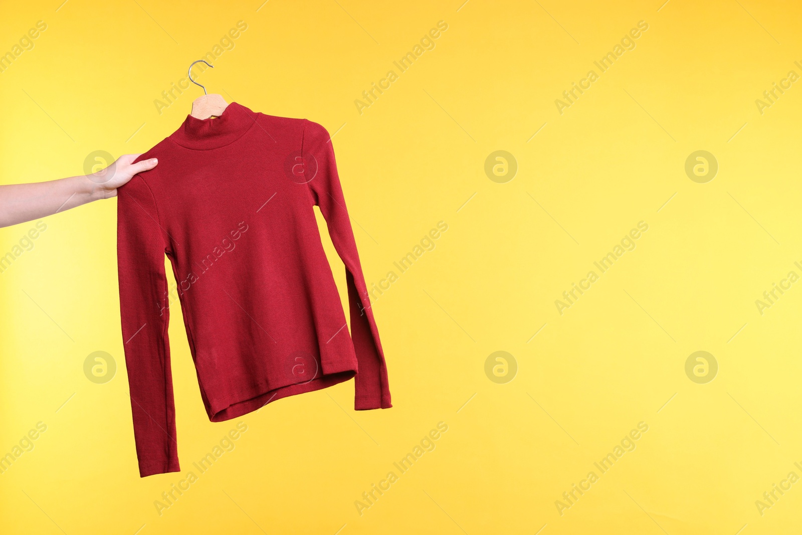 Photo of Woman holding hanger with red sweater on yellow background, closeup. Space for text