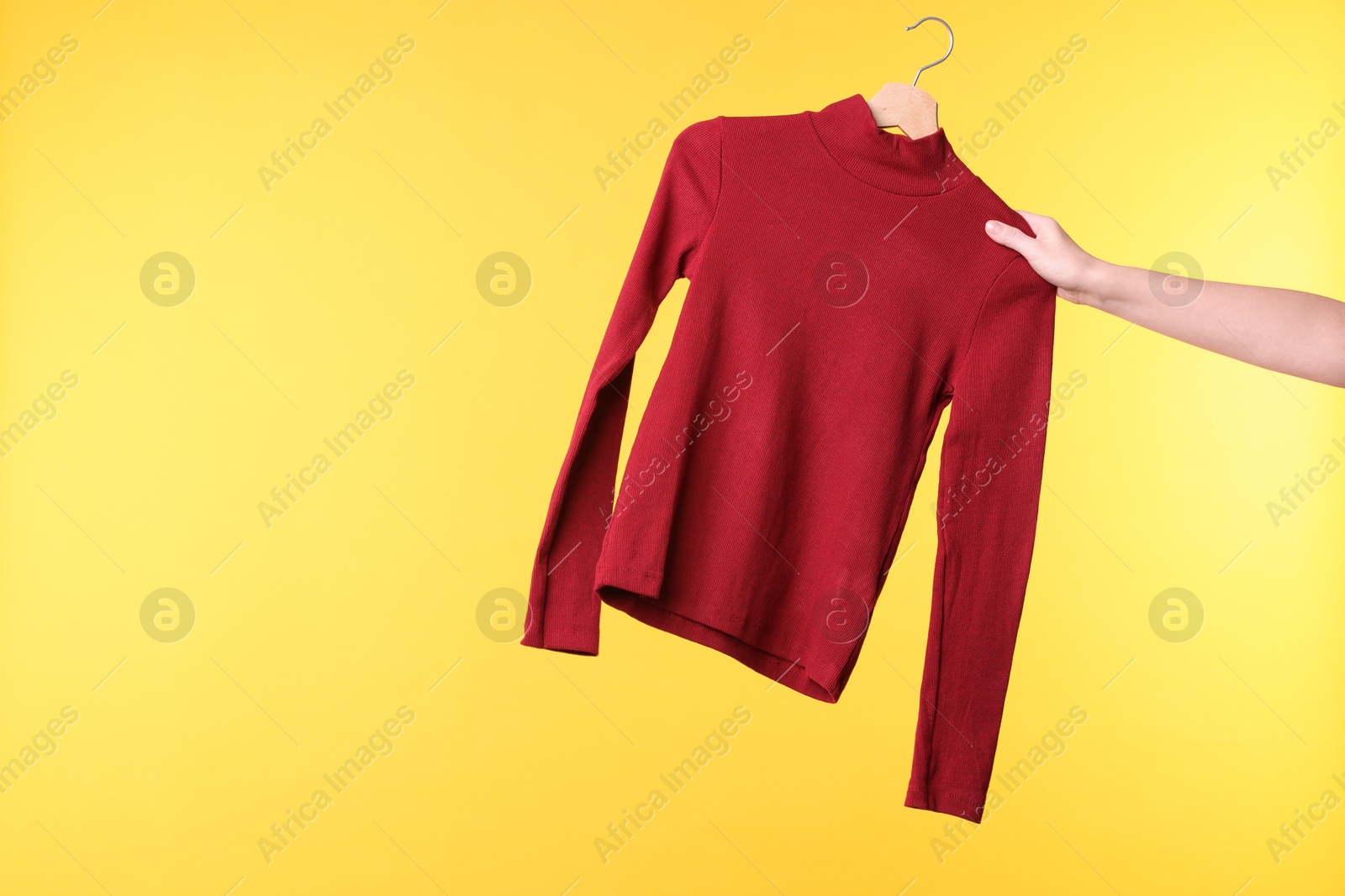 Photo of Woman holding hanger with red sweater on yellow background, closeup. Space for text