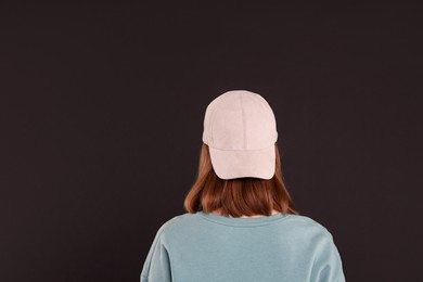 Photo of Woman in stylish baseball cap on black background, back view. Mockup for design