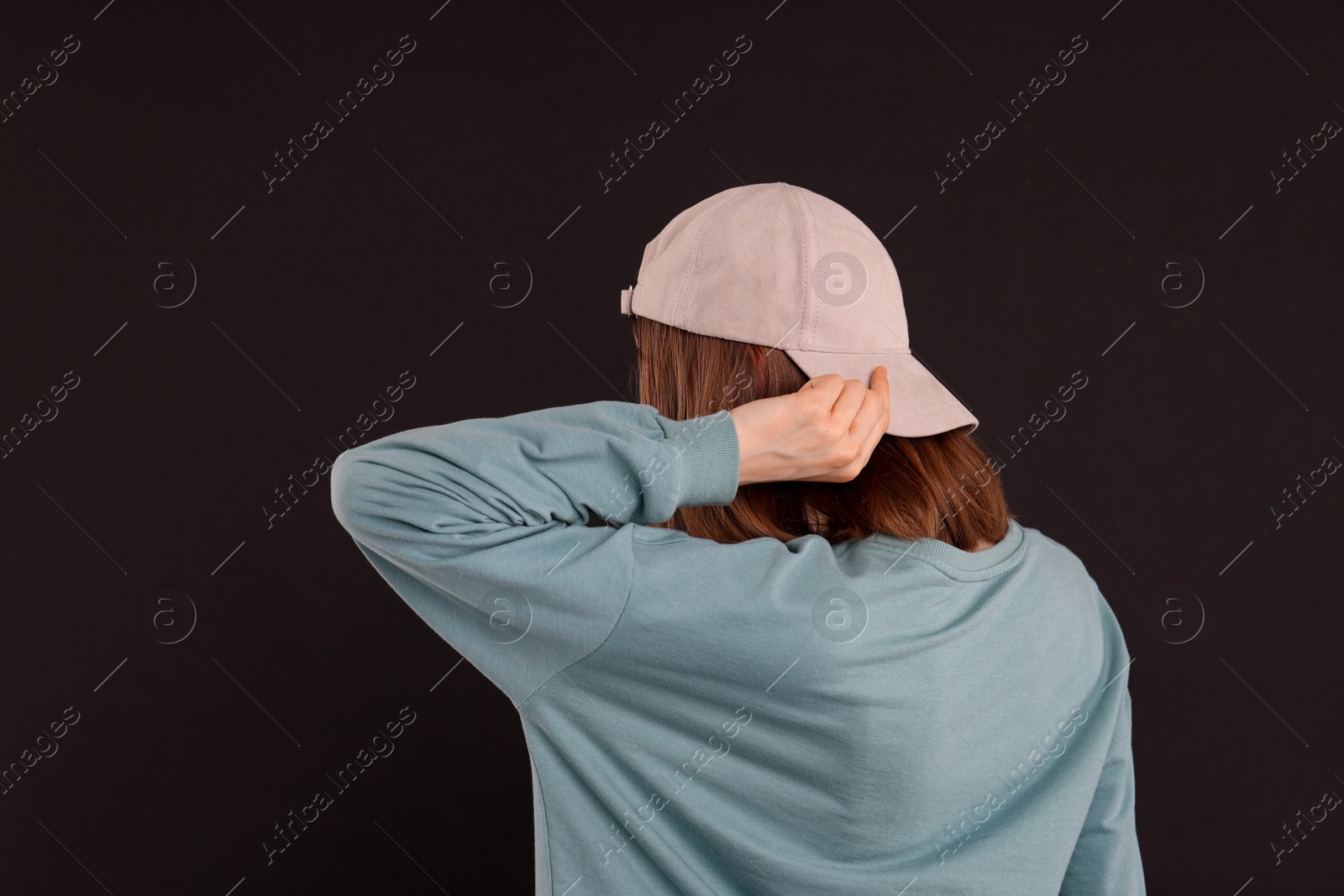 Photo of Woman in stylish baseball cap on black background, back view. Mockup for design