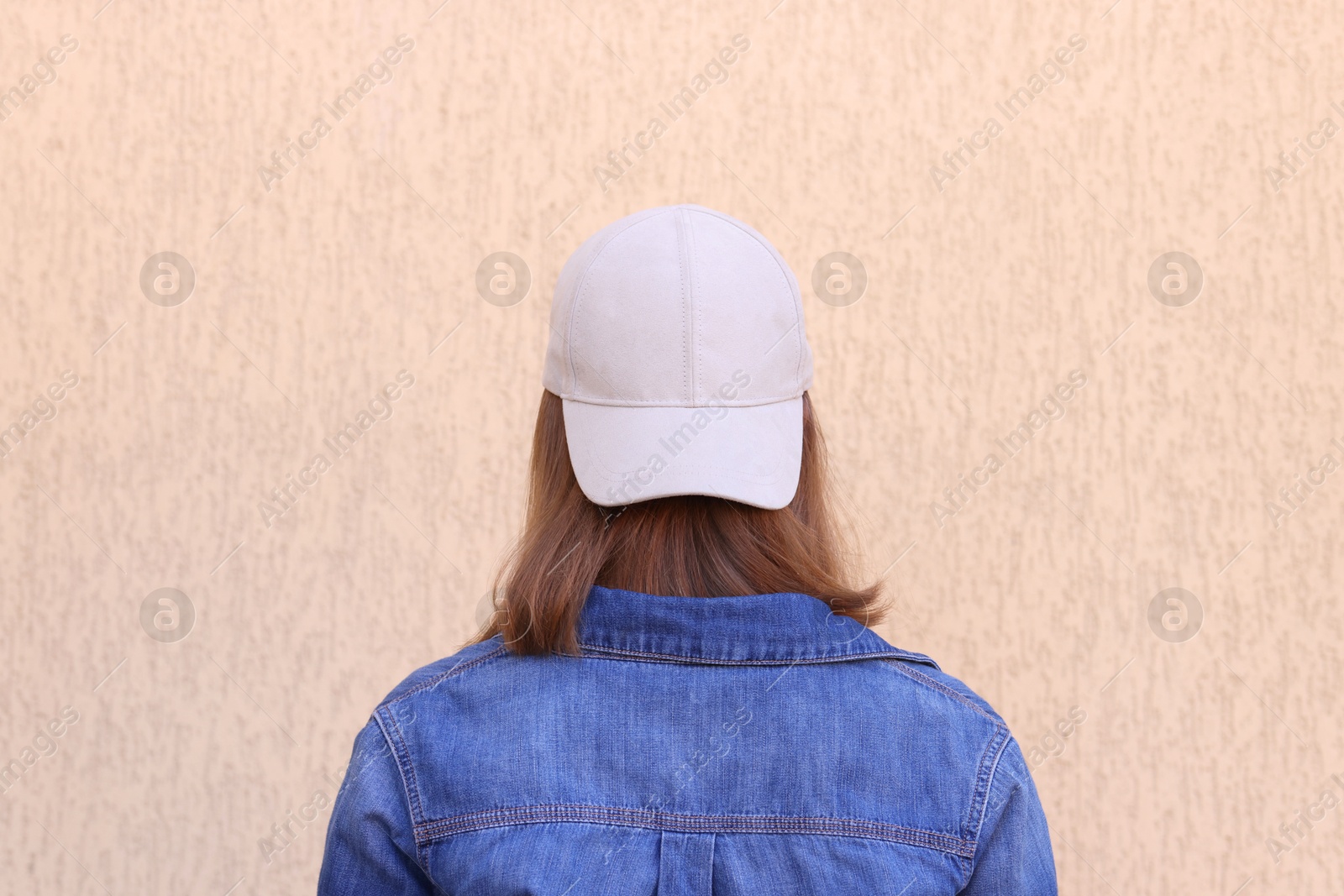 Photo of Woman in stylish baseball cap near beige wall, back view. Mockup for design