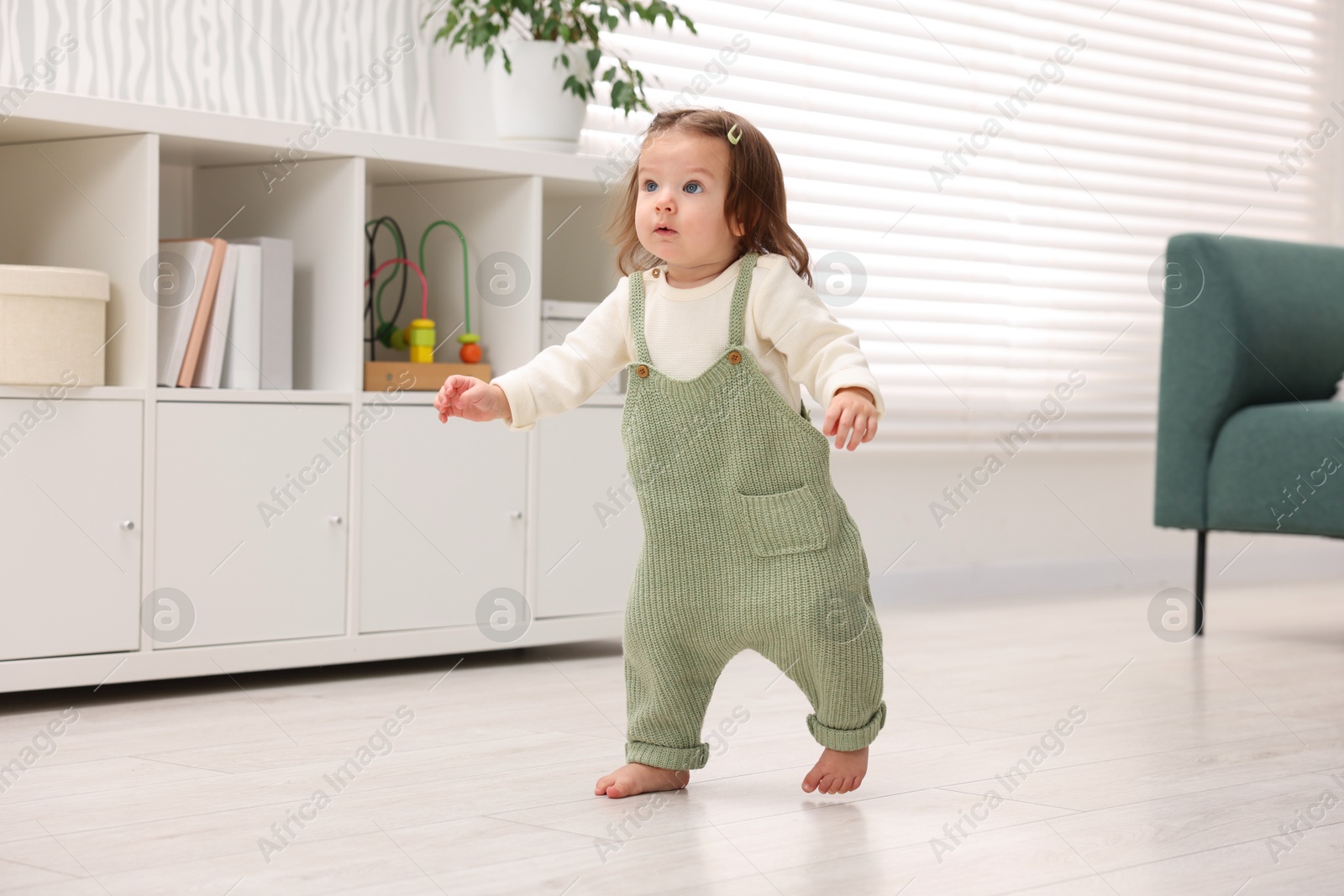 Photo of First steps. Cute little baby learning to walk at home