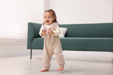 Photo of First steps. Cute little baby with toy learning to walk at home