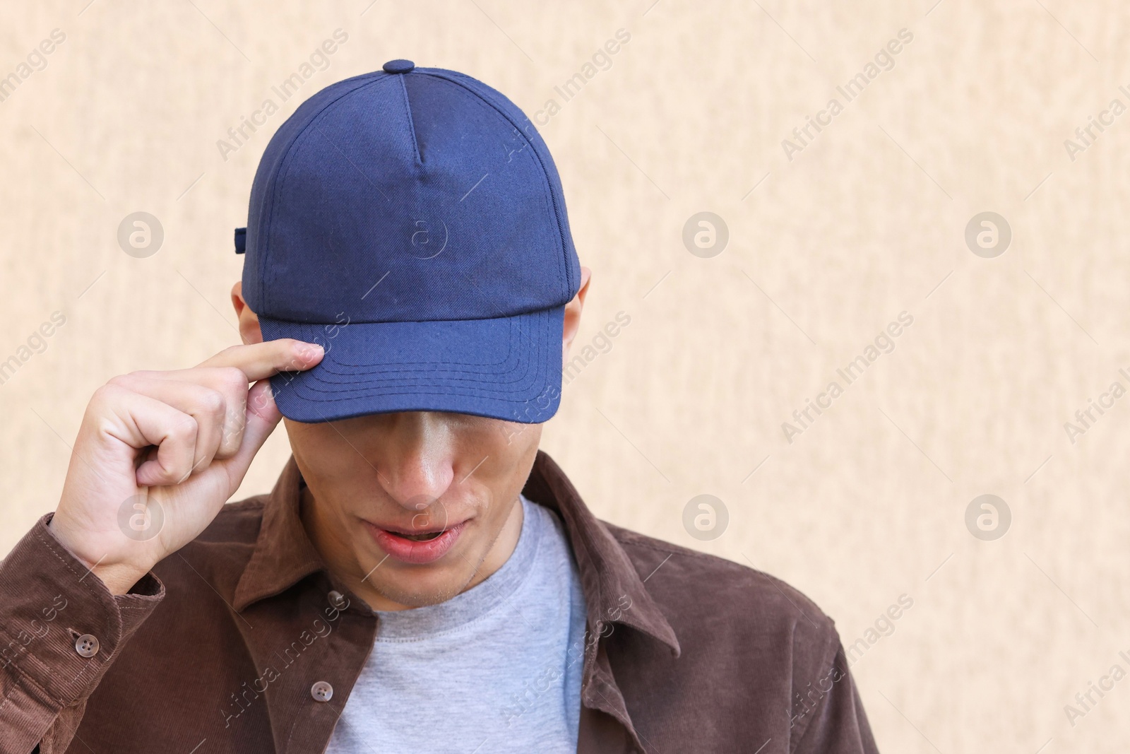 Photo of Man in stylish baseball cap near beige wall. Mockup for design