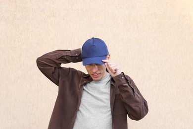 Photo of Man in stylish baseball cap near beige wall. Mockup for design