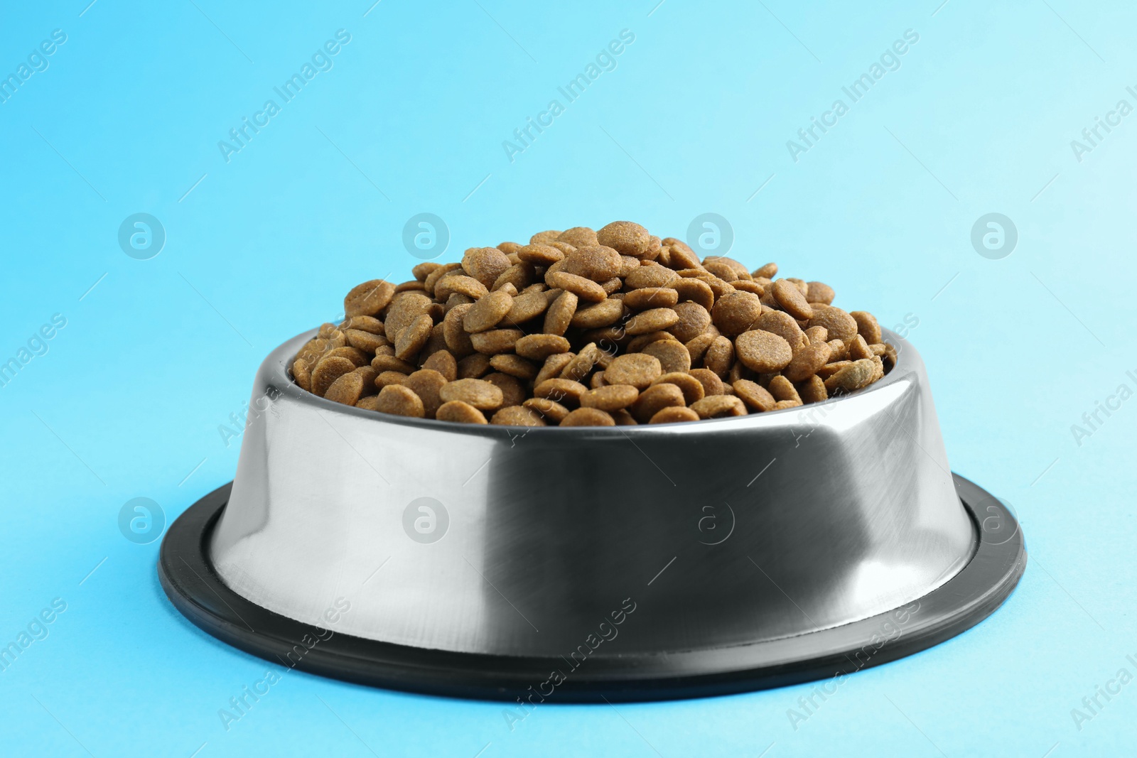 Photo of Dry pet food in feeding bowl on light blue background