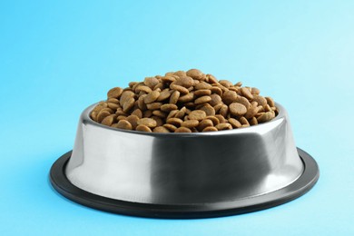 Photo of Dry pet food in feeding bowl on light blue background