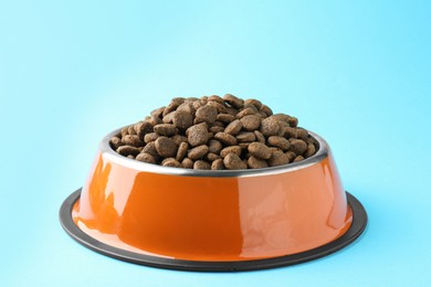 Photo of Dry pet food in feeding bowl on light blue background