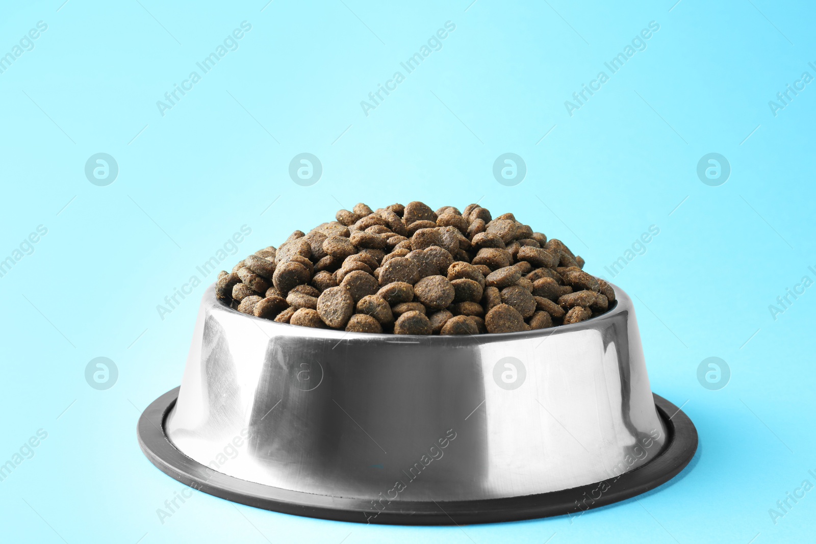 Photo of Dry pet food in feeding bowl on light blue background