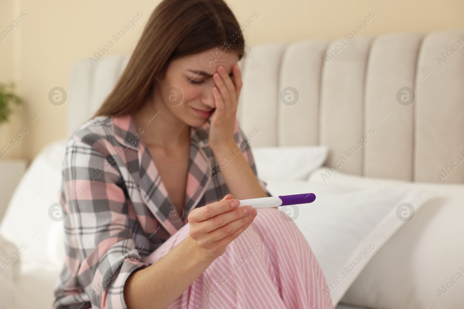 Photo of Upset woman with negative pregnancy test on bed at home, selective focus