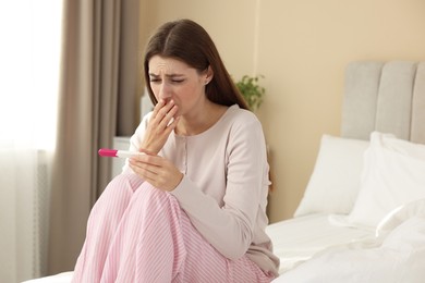 Photo of Upset woman with negative pregnancy test on bed at home